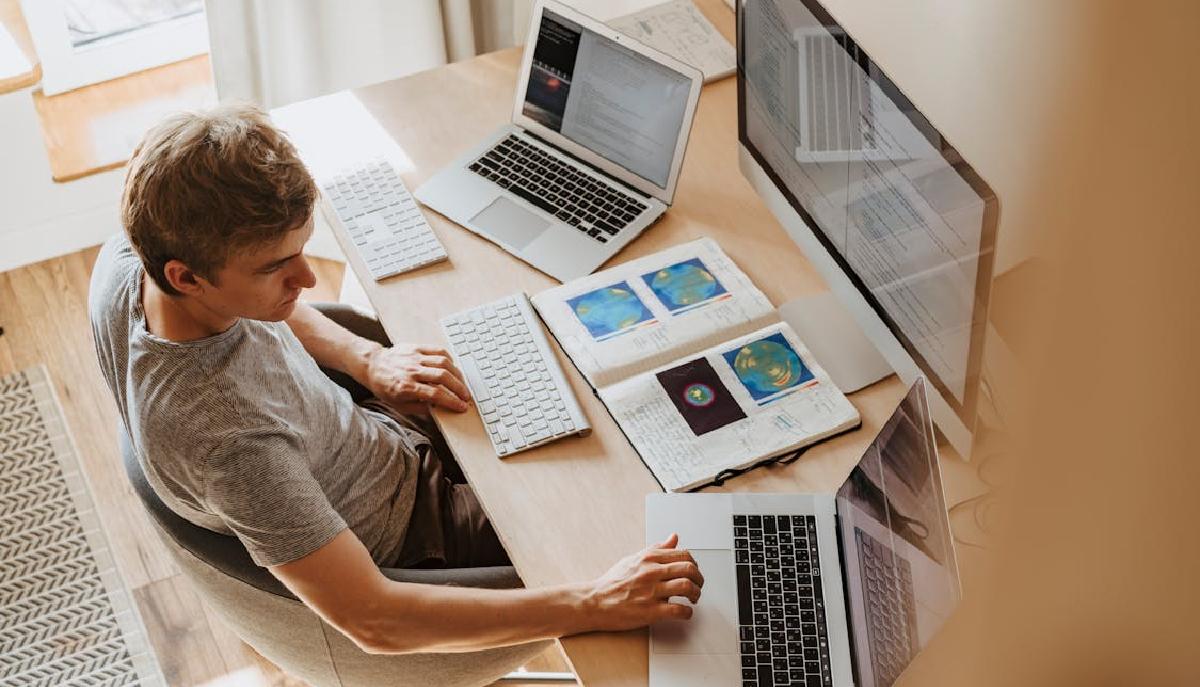 studente studia alla scrivania, sul banco da lavoro tre pc