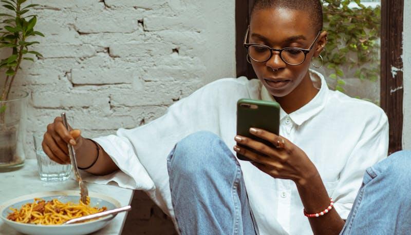 Ragazza seduta che legge dal cellulare mentre mangia