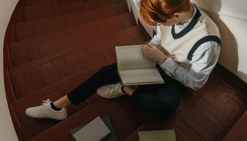 Studente che legge un libro seduto sulle scale