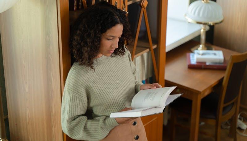 Studentessa che legge un libro poggiata a un armadio