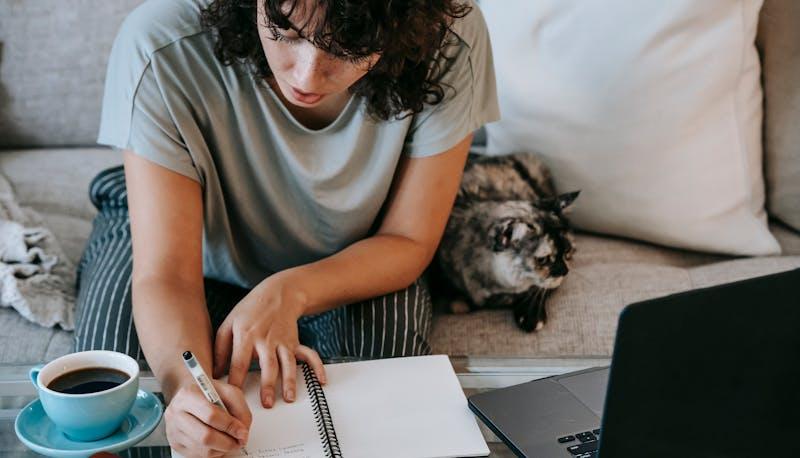 giovane donna studia al computer con caffè e gatto accanto