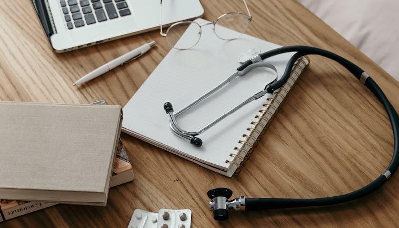 Quaderno, libri, computer, stetoscopio sulla scrivania di un candidato che studia per il test di Medicina
