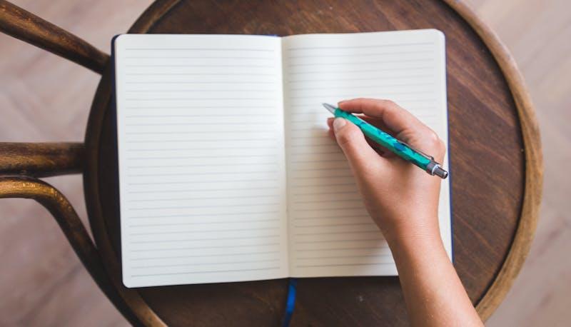 Studentessa di Chimica Materiali e Biotecnologie scrive su un quaderno poggiato sulla sedia per esercitarsi sulla seconda prova dell'esame di Stato