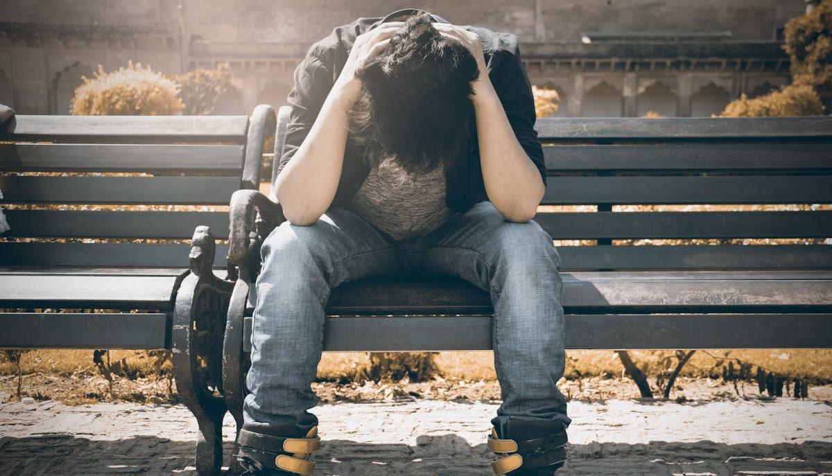 Ragazzo disperato seduto su una panchina mentre si tiene la testa tra le mani