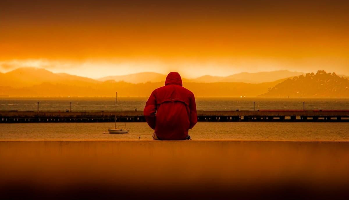 Ragazzo malinconico seduto in riva al mare, di spalle
