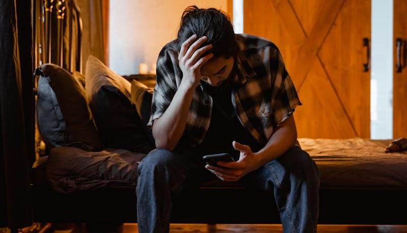Studente seduto sul letto, in preda alla disperazione per non essere andato bene al test di Medicina