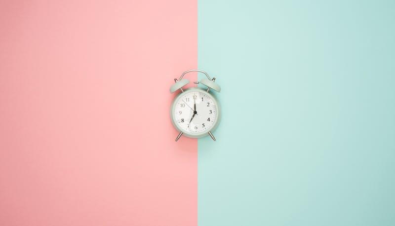 Una sveglia su sfondo rosa e verde, a simboleggiare il tempo
