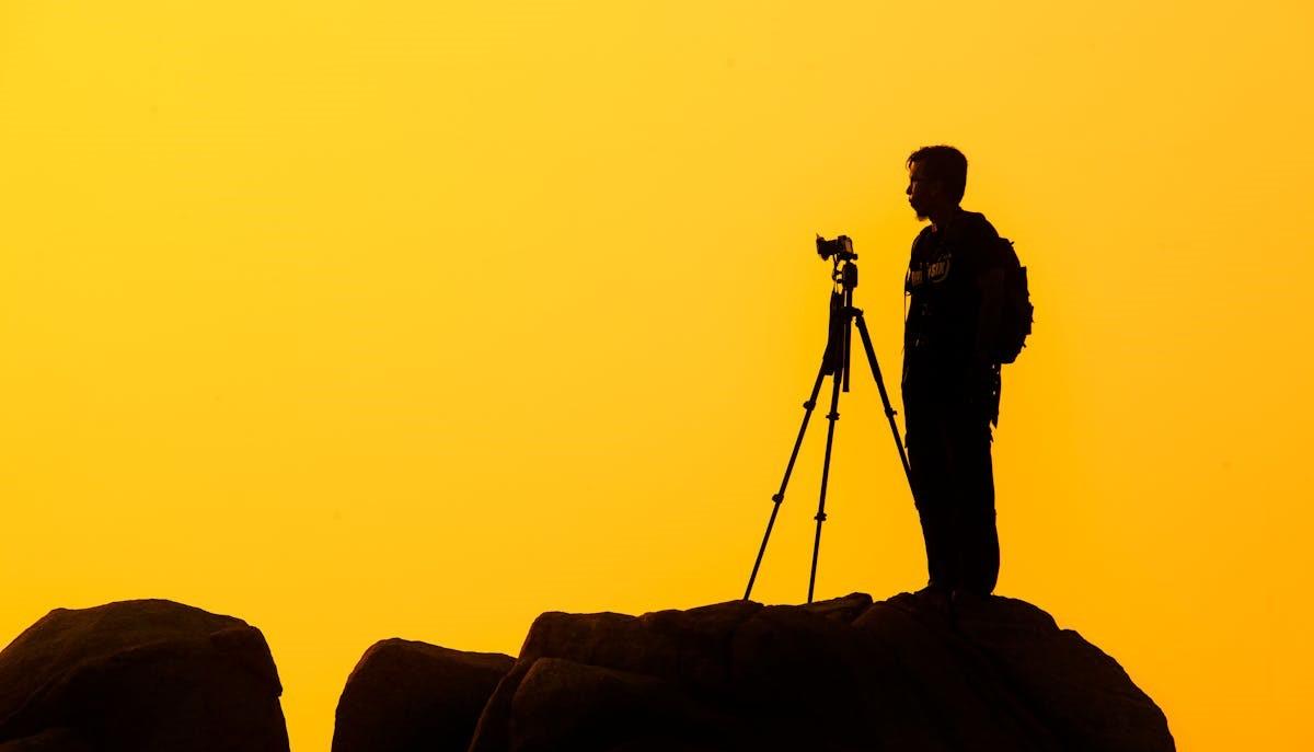 Uomo che fotografa con cavalletto su sfondo giallo