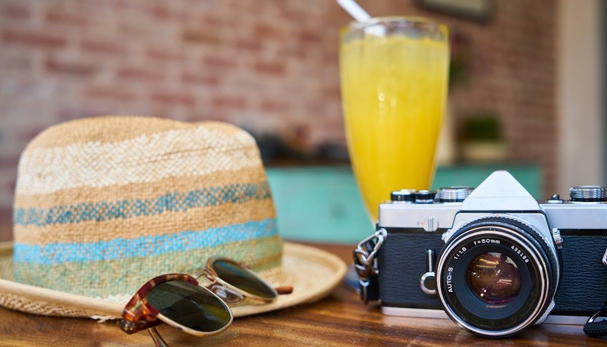 Occhiali da sole, macchina fotografica, cappello e bevanda fresca durante Ferragosto