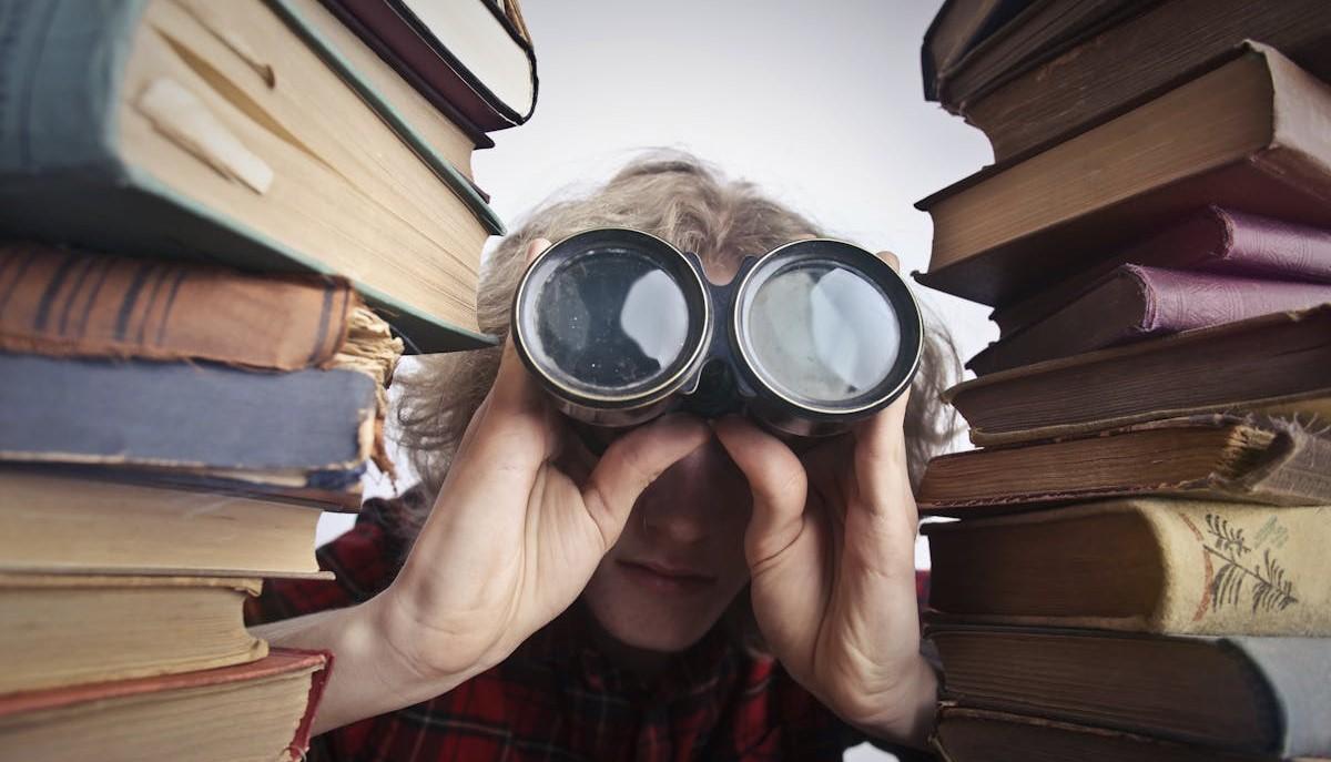 Studente in mezzo ai libri che guarda dal binocolo