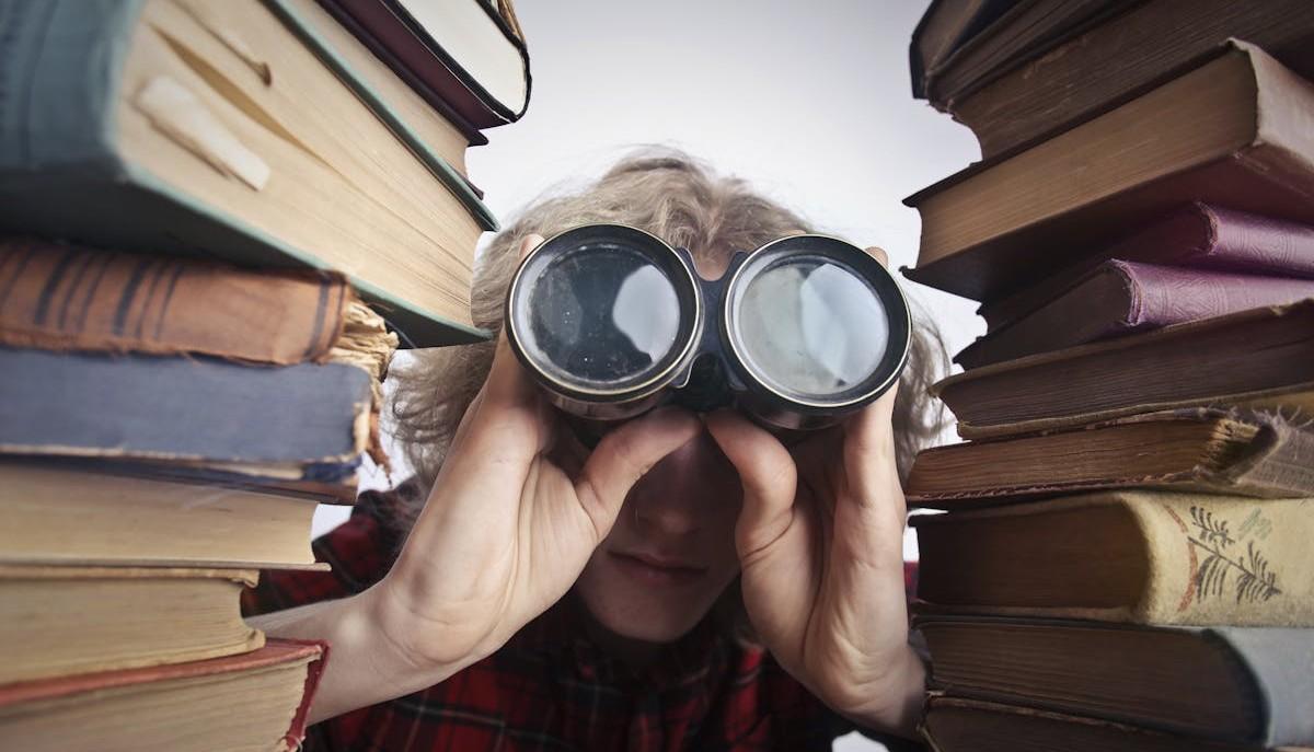 Studente con binocolo tra due pile di libri