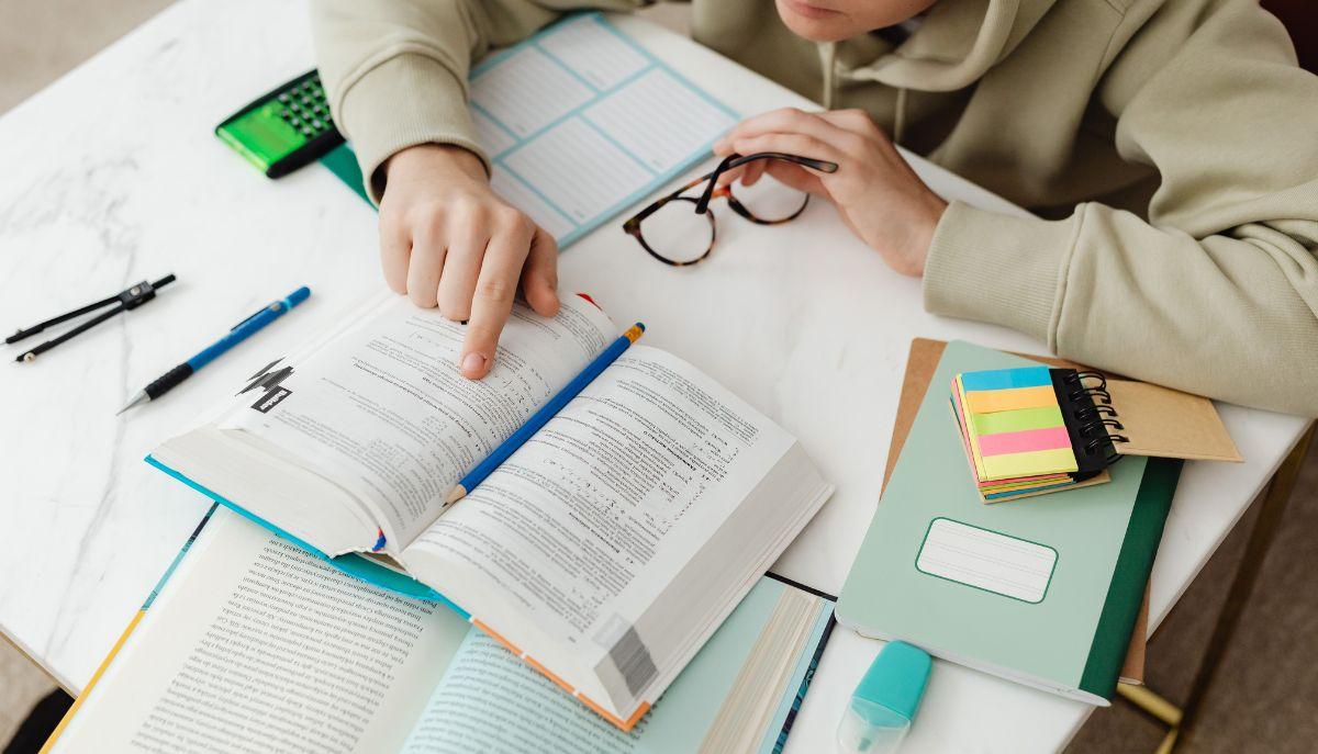 studente studia con diversi libri aperti sul tavolo davanti a lui