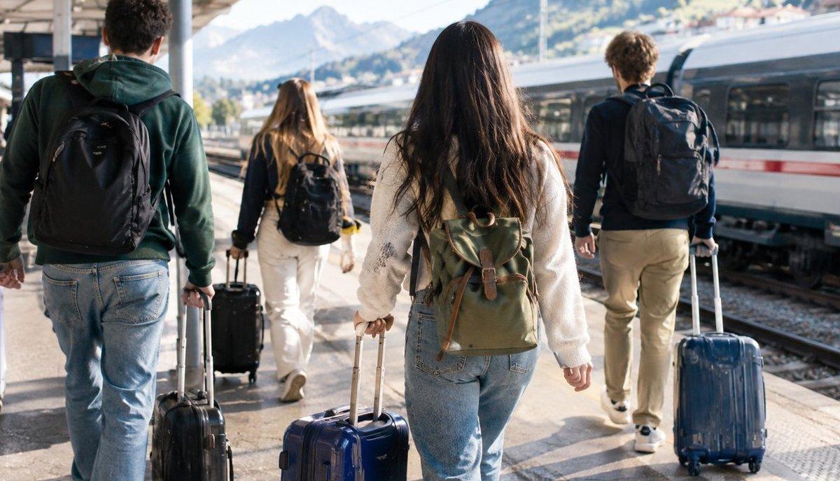 Illustrazione di quattro giovani con zaini e valigie che camminano sul binario verso un treno