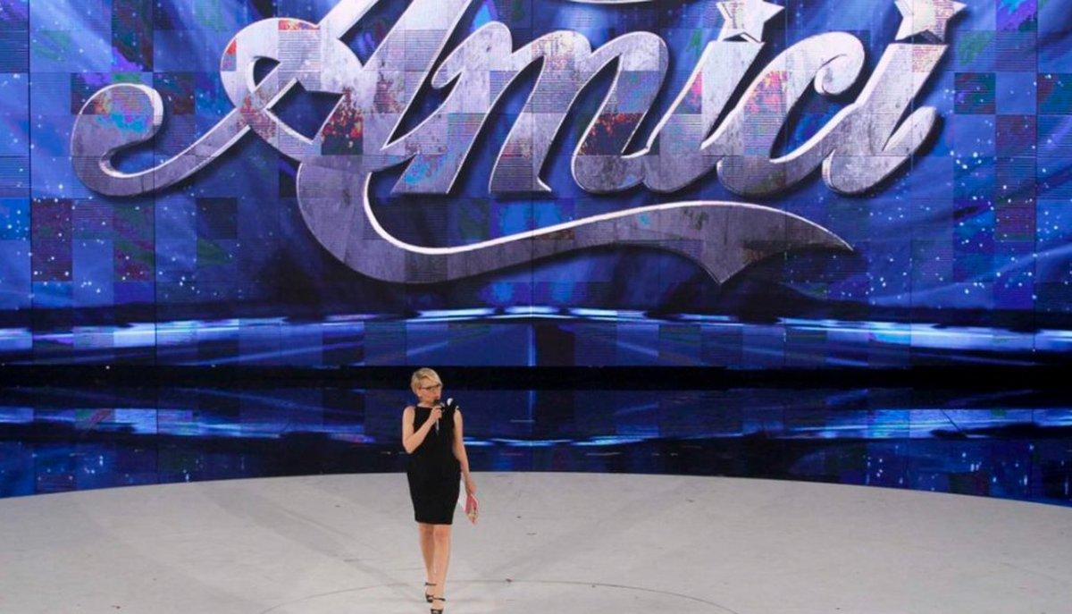 Una donna parla al microfono sul palco di Amici davanti al grande logo del programma