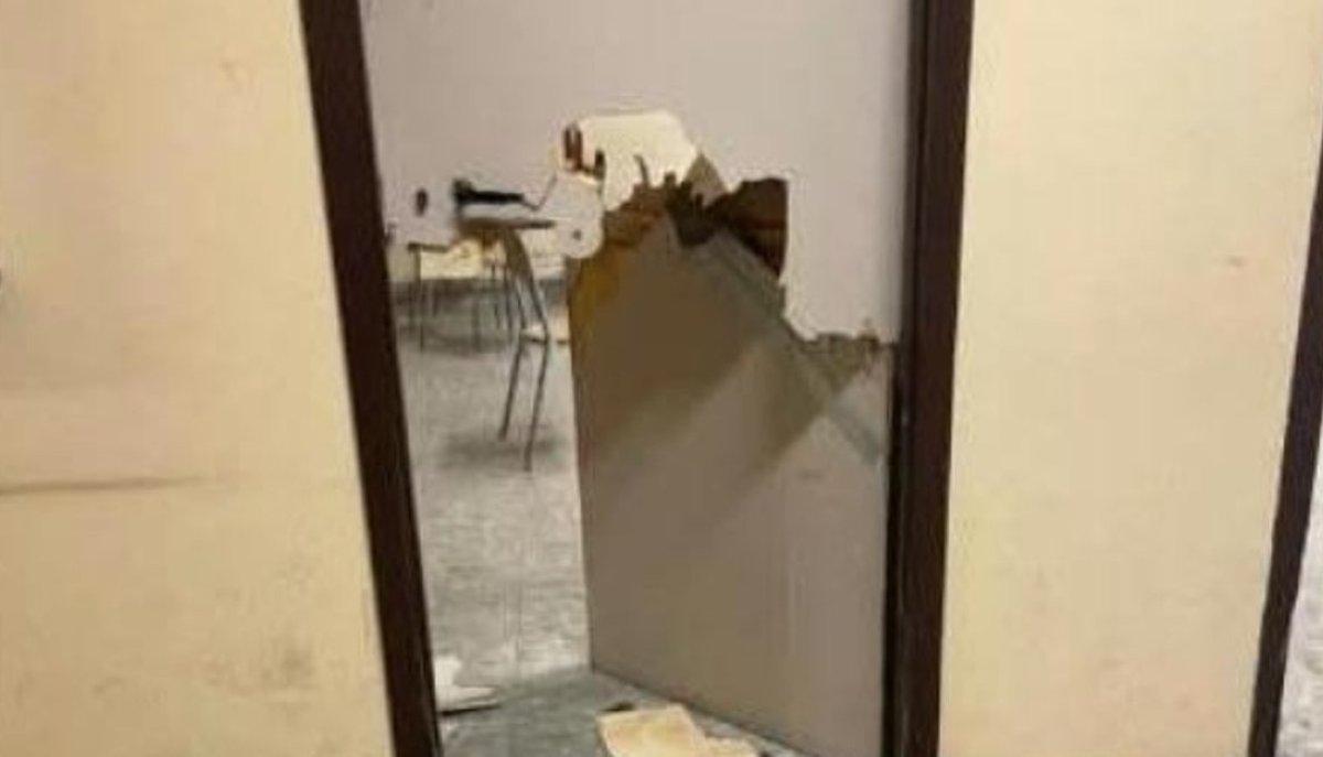 Porta di un'aula sfondata, con banchi visibili all'interno