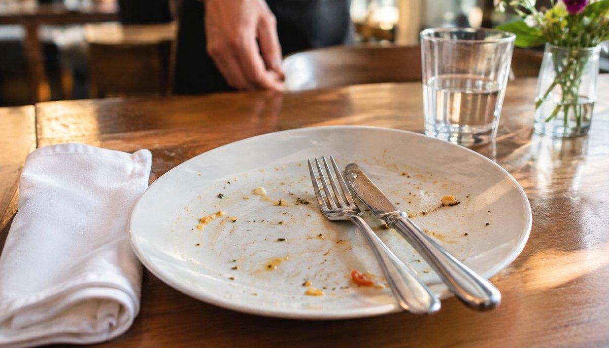 Illustrazione di un cameriere accanto a un piatto vuoto con posate su un tavolo di ristorante