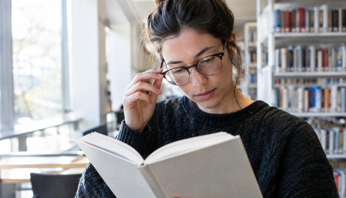 Illustrazione di una donna con occhiali che legge un libro in biblioteca