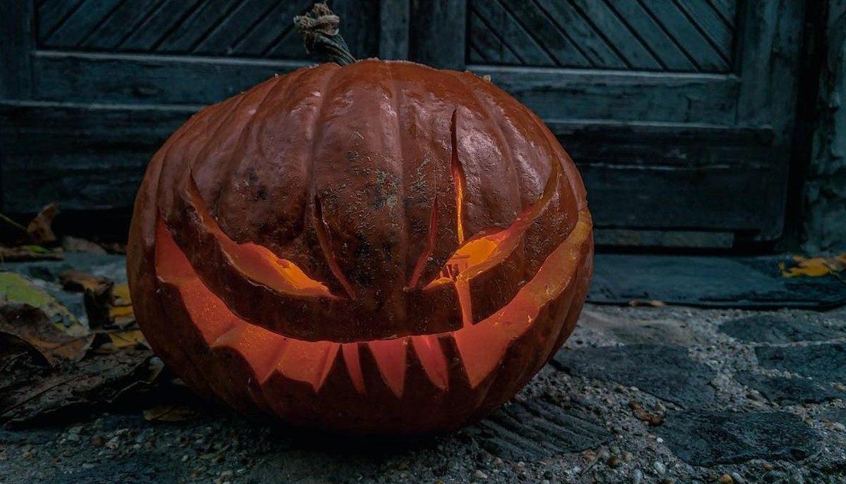 Zucca di Halloween intagliata con volto minaccioso e illuminata dall'interno davanti a una porta
